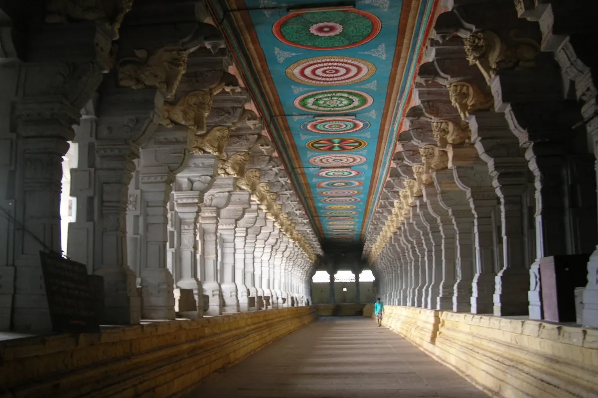 A single visitor walking the painted pillared corridor of the Ramanathaswamy Temple at Rameswaram, its ceiling covered in coloured medallions