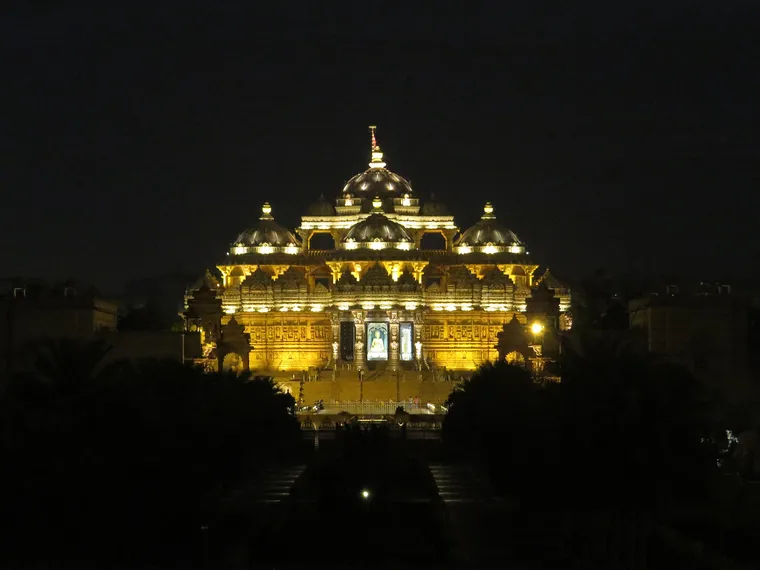 The carved domes and pillars of the Swaminarayan Akshardham mandir in New Delhi lit gold at night above dark gardens