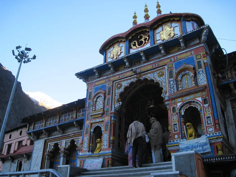 The brightly painted stone facade and arched gateway of the Badrinath Temple in early morning light, with pilgrims on the entrance steps