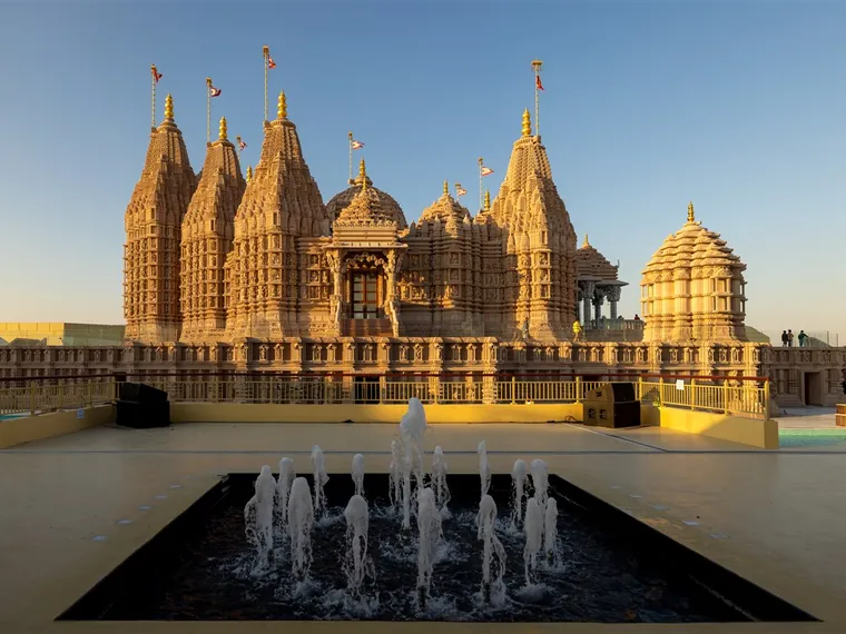 The seven carved stone spires of the BAPS Hindu Mandir in Abu Dhabi reflected in the water channel in front of it
