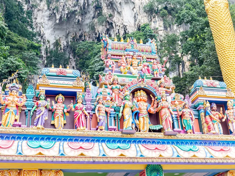 The gilded Murugan statue at Batu Caves beside the painted staircase leading up to the limestone cave temple