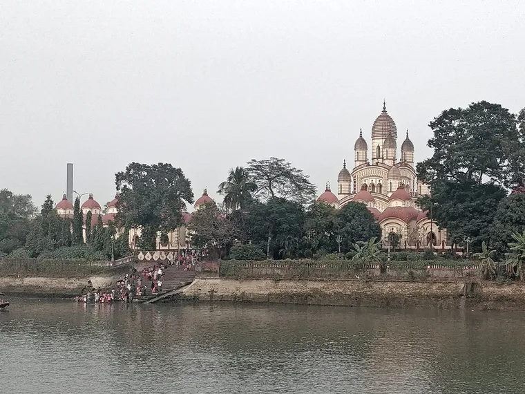 The nine-spired Dakshineswar Kali Temple and its row of smaller Shiva shrines seen across the Hooghly river, with bathers on the ghat steps