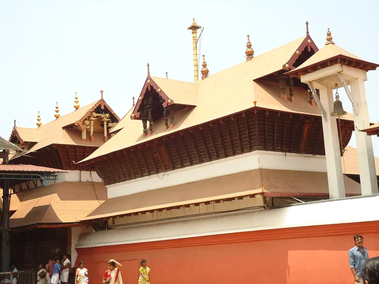 The copper-sheeted, tiered Kerala roofs and gold-covered flagstaff of the Guruvayur Sree Krishna Temple above its outer wall