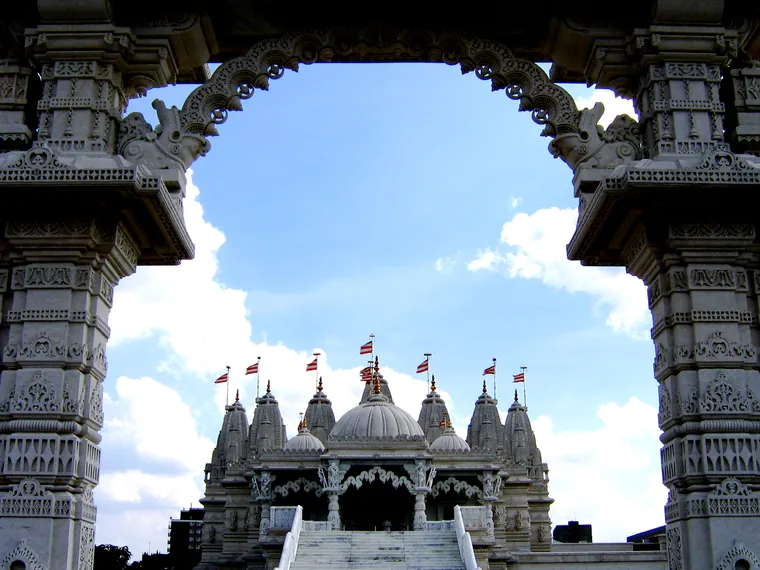 The carved gateway of the BAPS Shri Swaminarayan Mandir at Neasden in London framing the white marble mandir behind it