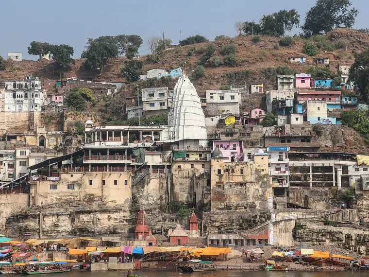 The white spire of the Omkareshwar Temple rising above houses and ghats on Mandhata island, seen across the Narmada