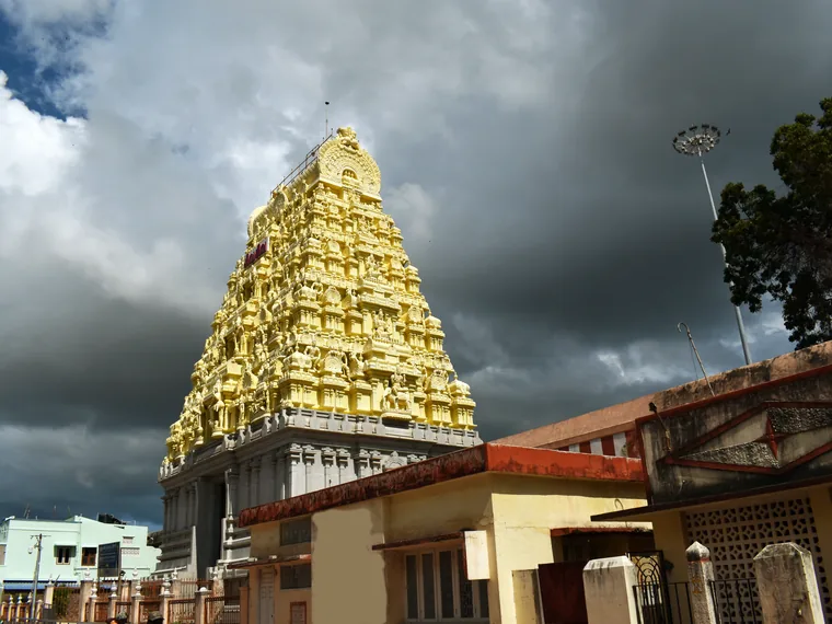A gilded, yellow-painted gopuram of the Ramanathaswamy Temple in Rameswaram rising above tiled rooftops under a dark sky