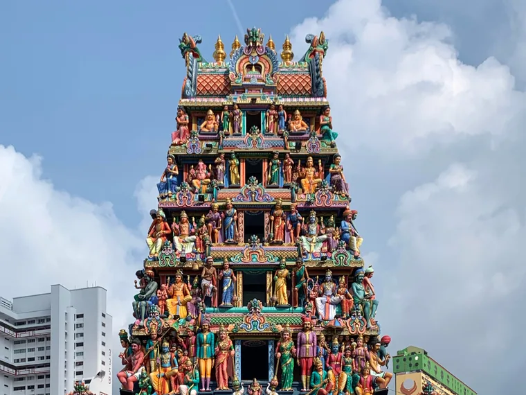 The upper tiers of the painted gopuram of Sri Mariamman Temple in Singapore, crowded with coloured figures of deities against a blue sky