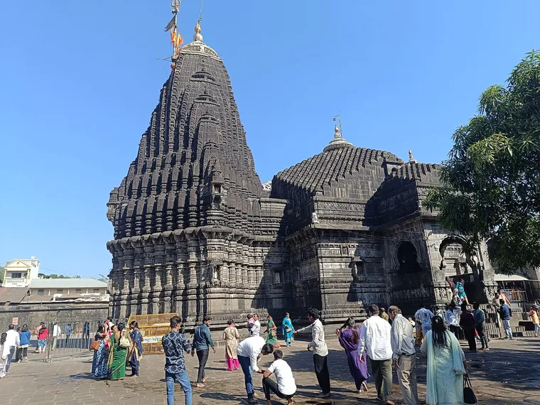 The black basalt shikhara and domes of the Trimbakeshwar Temple in Trimbak against a clear blue sky, with visitors in the stone courtyard